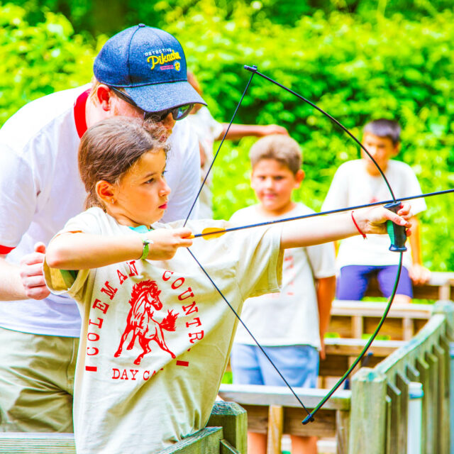 Counselor helping a camper with archery.