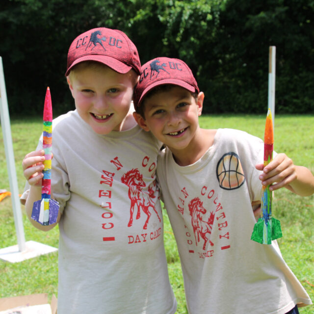 Two boy campers holding up their rockets in club