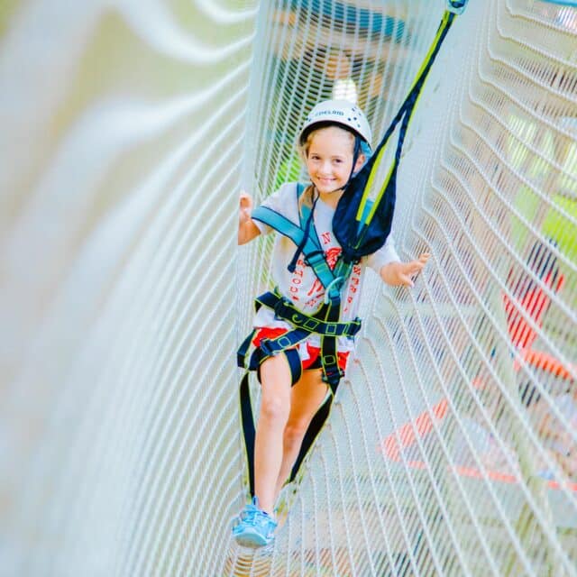 Explorers camper climbs through mesh on ropes course