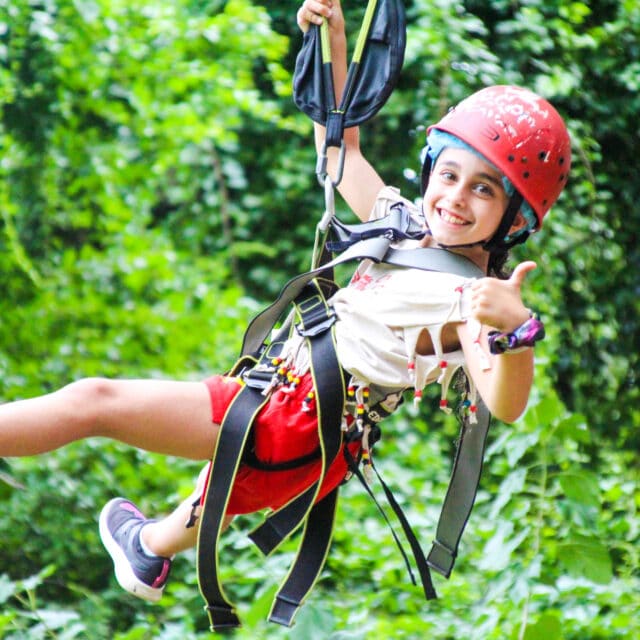 Scout camper giving a thumbs up on the zip line.