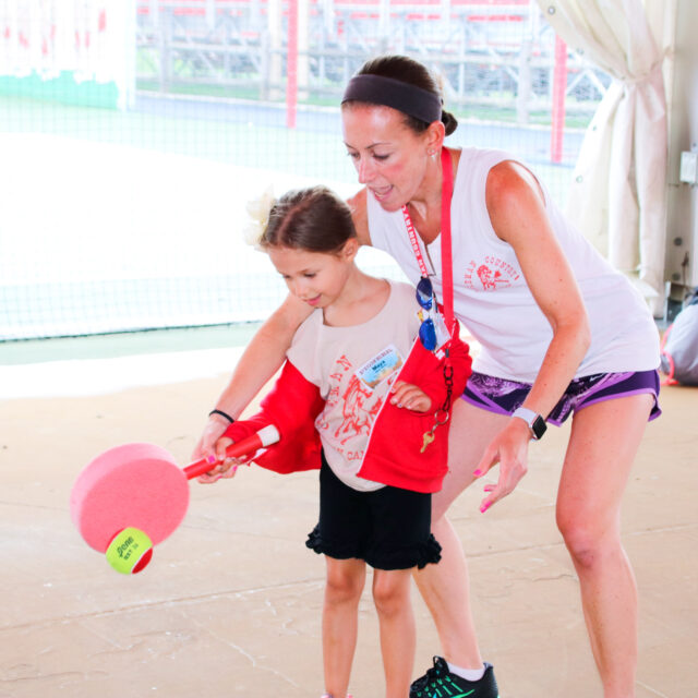 Tennis instructor teaching a girl camper how to hit the ball