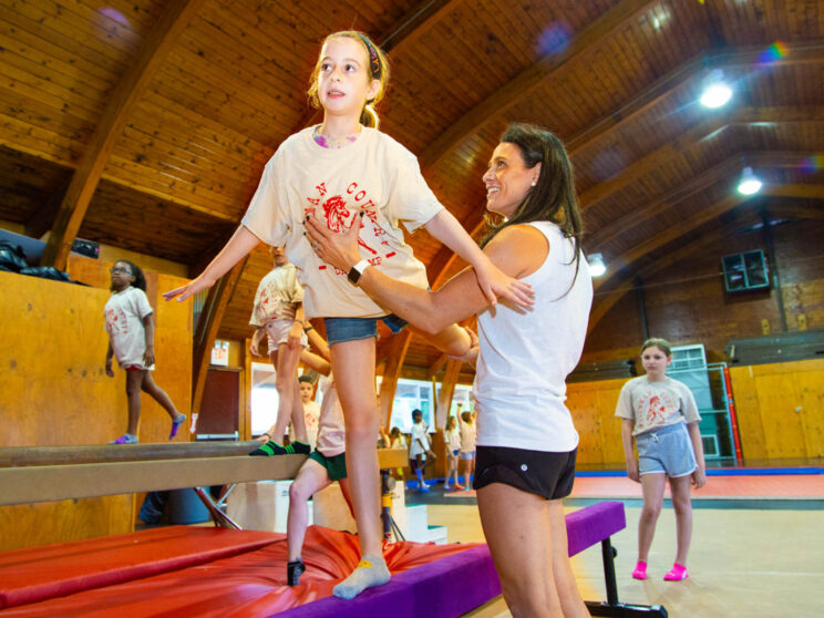 Instructor helps girl balance on beam at camp