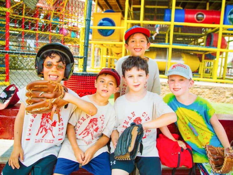 Four boys with baseball gloves smiling together at camp