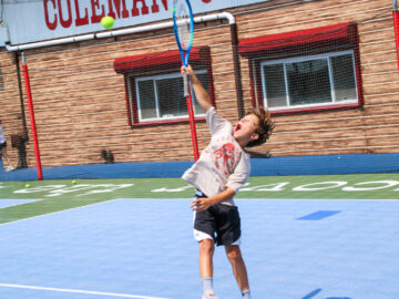 Camper reaching for a tennis ball with his raquet.