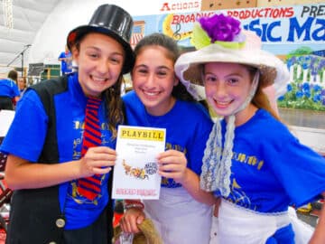 Campers in costume holding up a playbill for their musical.