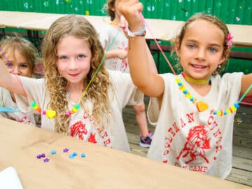 Two campers hold up craft necklaces