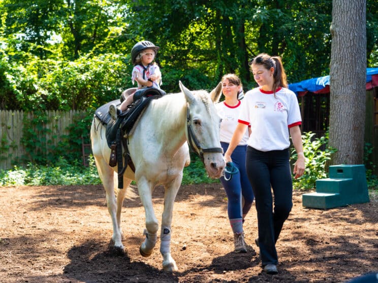 Camper on a horse with counselors leading the horse.