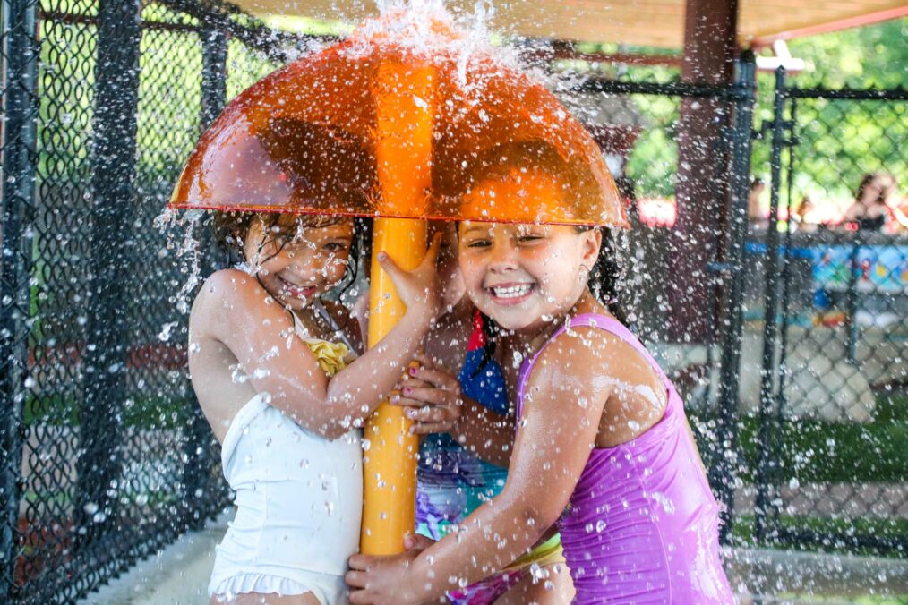 Two girl campers standing under a water feature at the waterpark