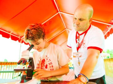 Boy looking into a microscope with counselor