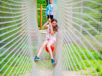 Camper swings on rope across netting