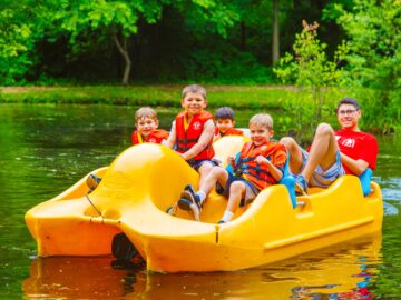 Group of campers drive pedal boat across pond