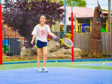 Smiling girl plays tennis at camp