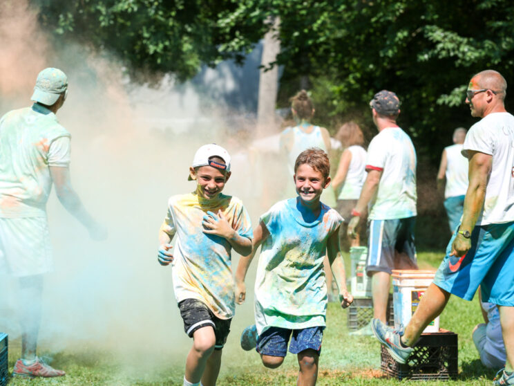 Two boy campers running and getting color thrown at them