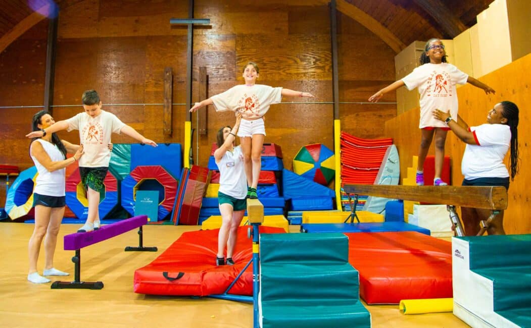 Three counselors help campers on balance beams