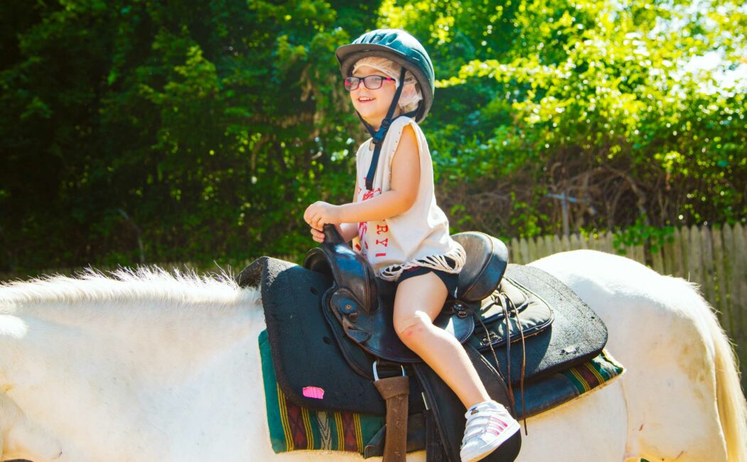 Smiling young camper rides horse