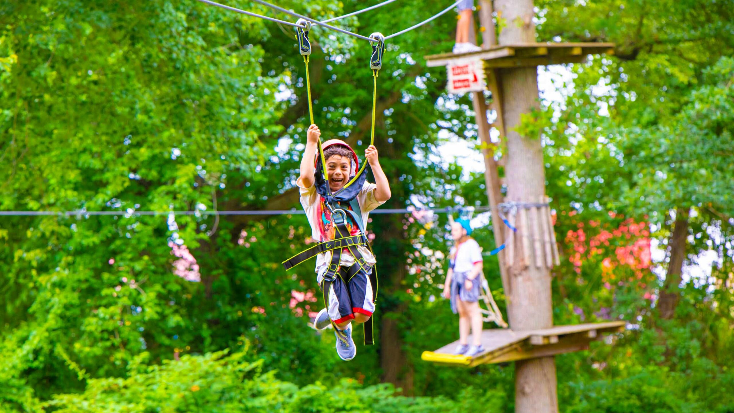 Young camper ziplines through forest canopy