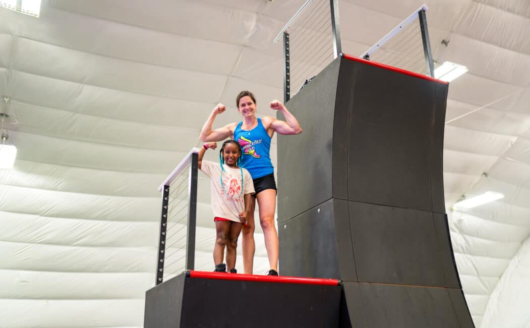 Flex Labrek standing with a girl camper on a high platform