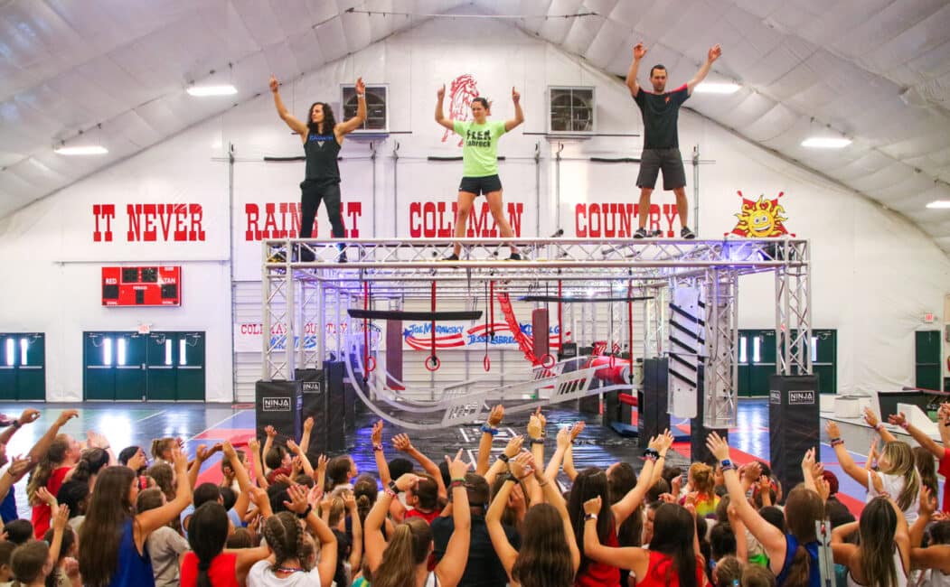 American Ninja Warrior's Daniel Gil, Joe Moravsky, and Flex Labrek standing on a high platform in front of a large group of campers