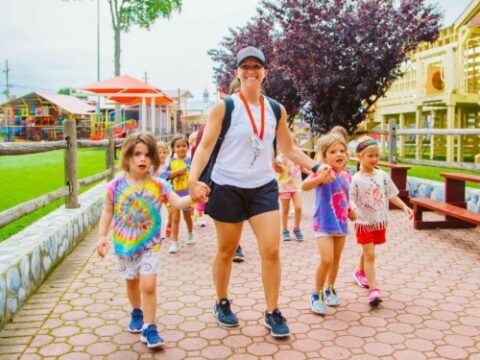 Smiling counselor walking campers on a path at camp