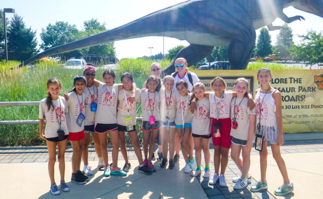 Group of girl campers in front of a dinosaur statue