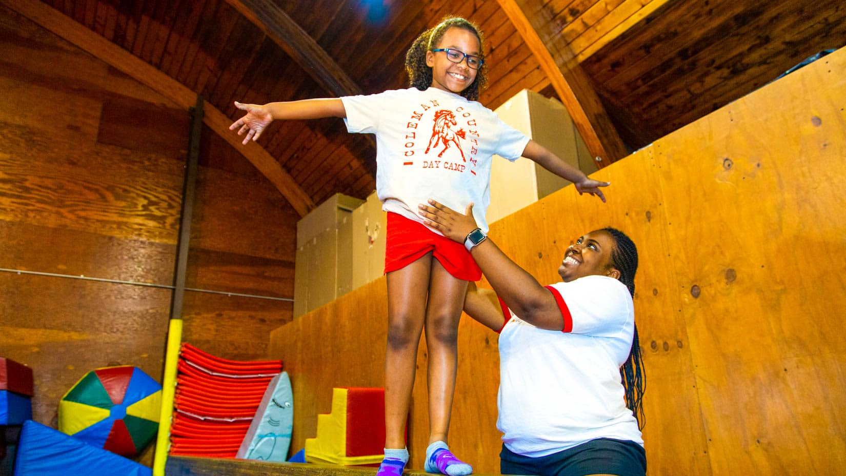 Camper on the balance beam with the assistance of a counselor.